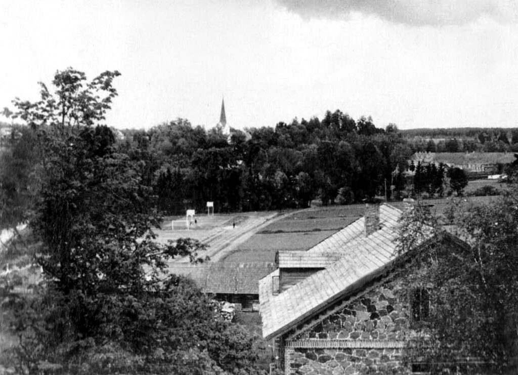 Skats no Krievkalna baznīcas torņa uz Kokneses vidusskolas ēku un sporta laukumu, tālumā labajā pusē redzama otra skolas ēka – “Saules”, 1960. gads. Nezināma autora fotouzņēmums.