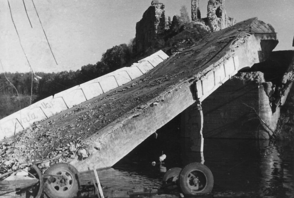 Saspridzinātais Pērses tilts, priekšplānā kinofilmas “Noktirne” uzņemšanas epizodē no tilta nogāztā sanitārā mašīna, 1965. gada oktobris. Gunāra Magones fotoattēls.
